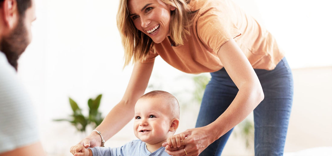 Woman smiling and holding babies hands walking to dad