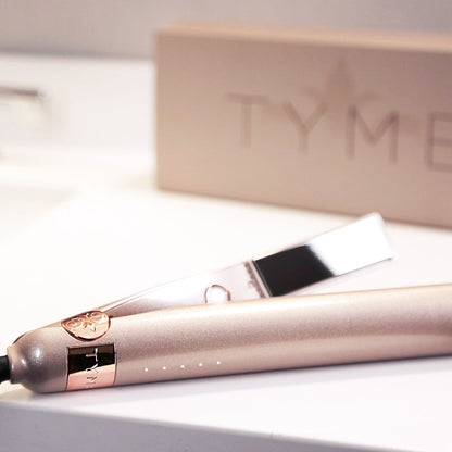 Champagne pink metallic TYME Iron Pro with rose gold details with product box featuring TYME LLC logo in the background.